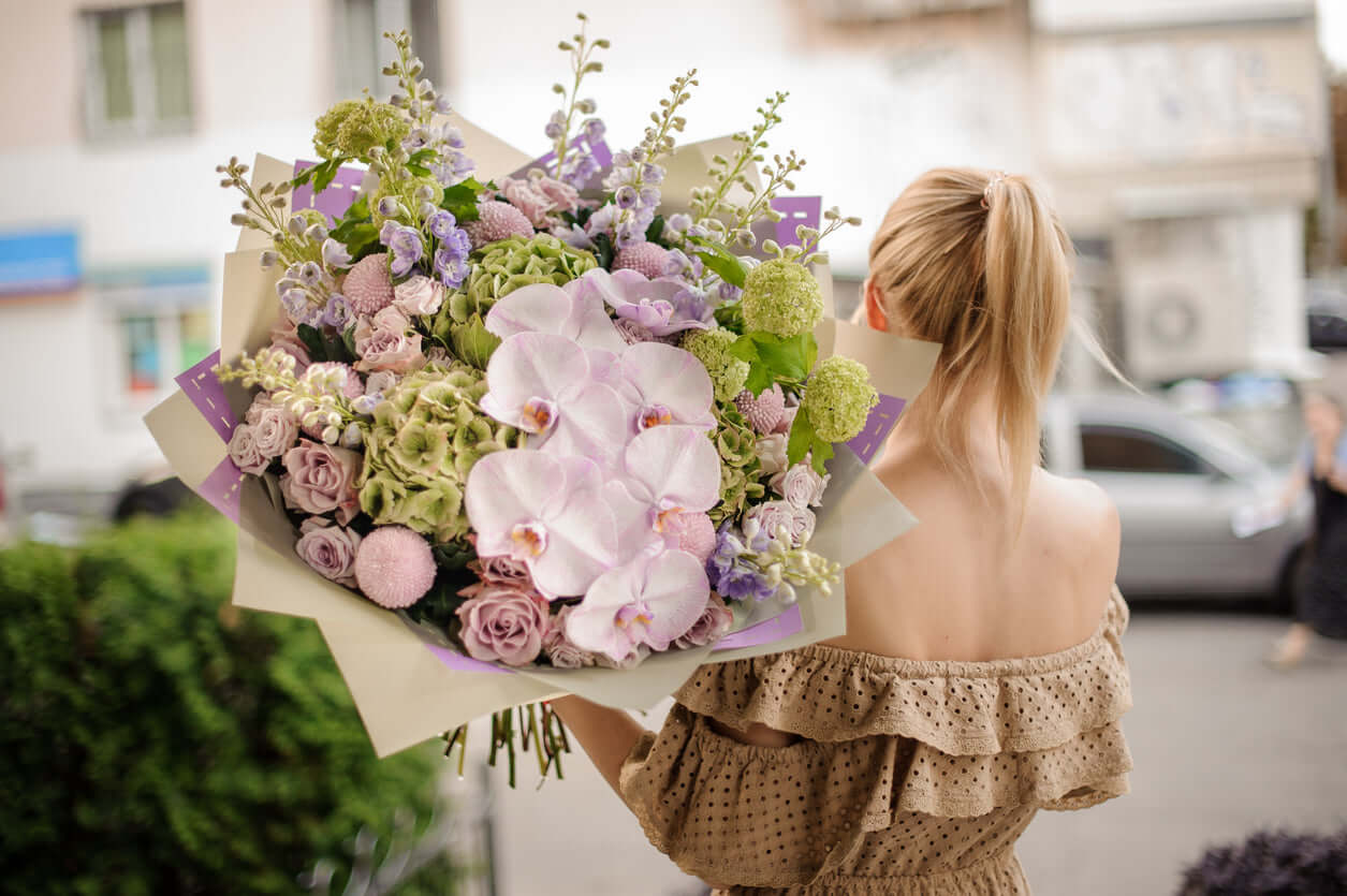 Strauß "Dany" in buntem Blumenarrangement mit Phalaenopsis-Orchideen und Rosen, gehalten von einer Person.